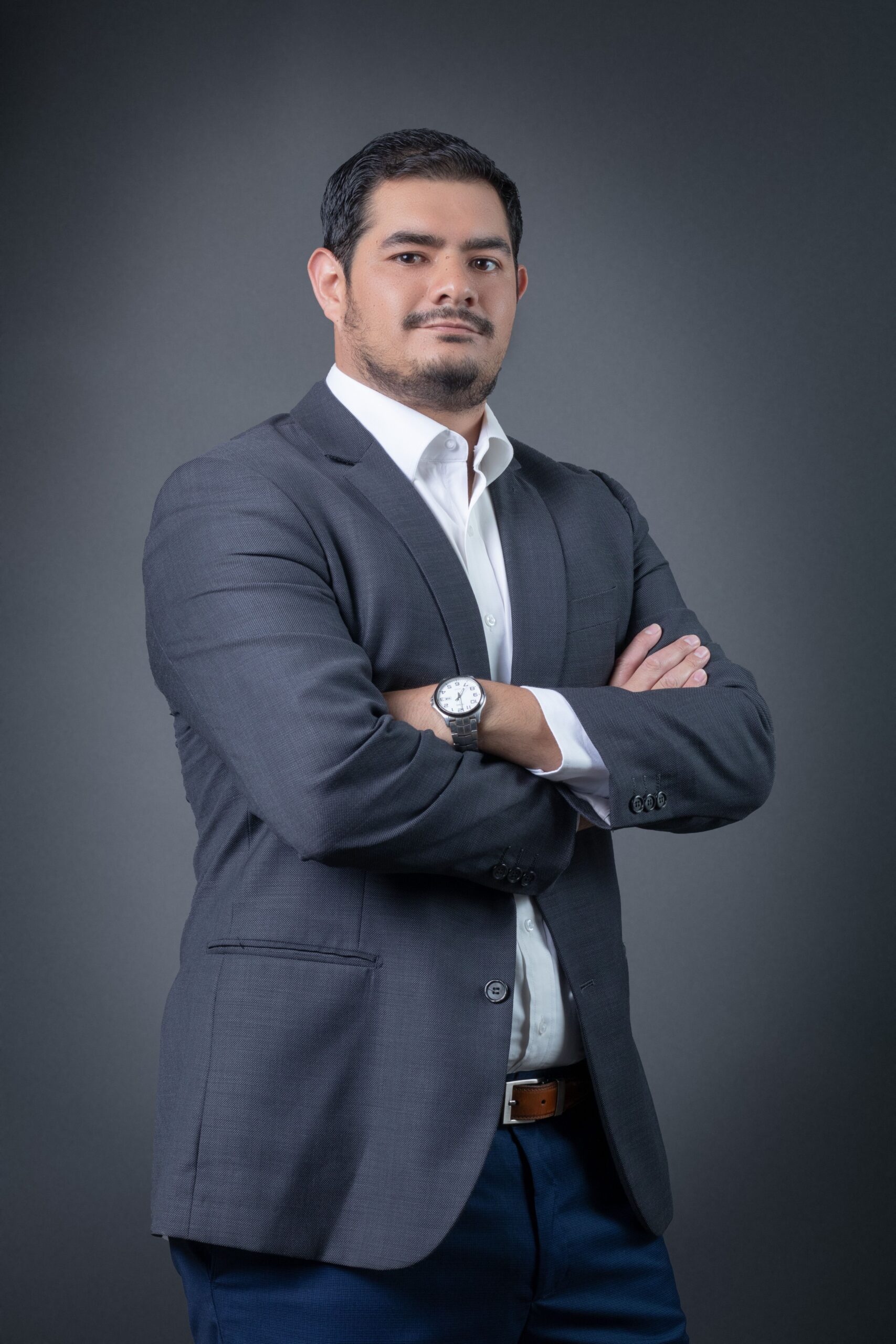Portrait of a confident man in a gray business suit with arms crossed against a gray background.